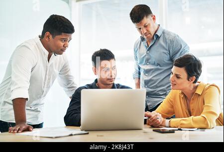 Ils passent en revue toutes les options dont ils disposent. Un groupe d'hommes d'affaires travaillant ensemble sur un ordinateur portable dans un bureau. Banque D'Images