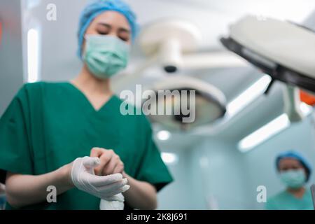 Portrait d'un chirurgien asiatique avec un masque médical debout et portant des gants médicaux dans une salle d'opération à l'hôpital. Équipe de chirurgiens professionnels. Hé Banque D'Images
