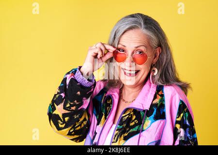 L'âge est un sentiment, pas un certain nombre d'années. Portrait d'une femme âgée confiante et élégante portant des lunettes de soleil se posant sur un fond jaune. Banque D'Images