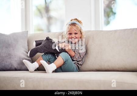 Je pouvais jouer avec mes jouets toute la journée. Portrait d'une adorable petite fille assise seule sur le canapé et jouant avec ses jouets à la maison. Banque D'Images