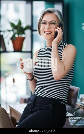 Vous obtiendrez toujours de bonnes nouvelles si vous êtes bien à ce que vous faites. Une femme d'affaires ayant le café tout en parlant sur son téléphone portable dans son bureau. Banque D'Images