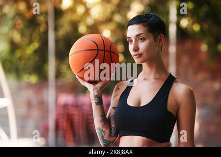 Déplacez-vous sur les garçons, laissez une fille vous montrer comment jouer. Une jeune femme sportive tenant un basket-ball sur un terrain de sport. Banque D'Images