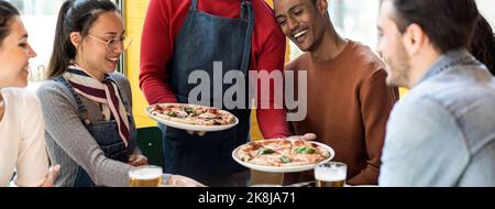 Bannière horizontale ou en-tête avec serveur servant de délicieuses pizzas margherita à des amis multiculturels dans le restaurant pizzeria confortable - amis multiethniques Banque D'Images