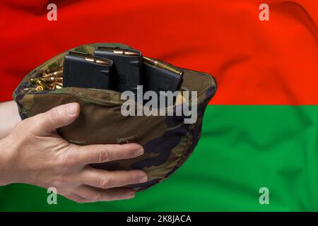 Un casque militaire avec cartouches et magazines pour un fusil dans les mains d'un homme sur fond du drapeau du Burkina Faso. Le concept de Banque D'Images