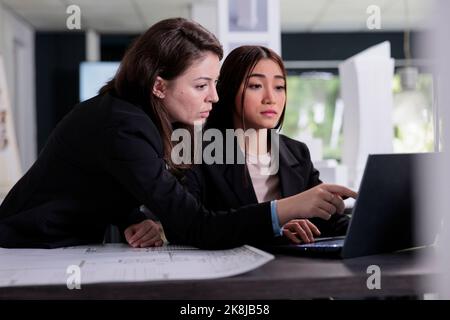 Architectes travaillant avec le logiciel de CAO, discutant des plans architecturaux dans l'espace de travail des collègues. Employés dans un bureau d'architecture au bureau de travail, projet de construction d'agence immobilière. Banque D'Images