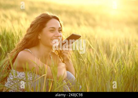 Bonne femme utilisant la reconnaissance vocale sur un smartphone dans un champ de blé au coucher du soleil Banque D'Images