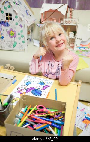 Une fille blonde peint un dessin d'une licorne dans un livre de coloriage pour enfants. Un enfant joyeux est engagé dans les beaux arts Banque D'Images