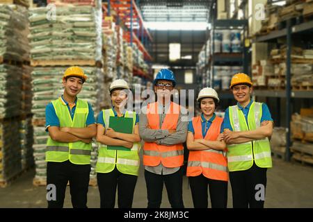 Groupe d'employés d'entrepôt en casque et veste réfléchissante debout avec bras croisés et regardant avec confiance la caméra Banque D'Images