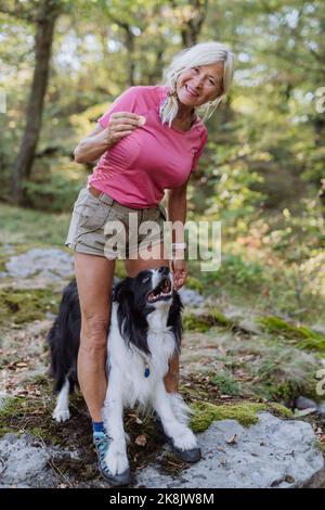 Femme âgée formant son chien pendant une promenade dans la forêt. Banque D'Images