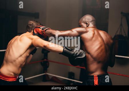 Deux boxeurs multiraciaux qui lancent des coups de poing lors d'un combat dans un ring de boxe. Deux jeunes hommes sportifs ayant un match de boxe dans une salle de fitness. Banque D'Images