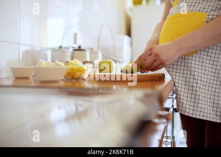 Gros plan de la femme enceinte de race blanche en tablier coupant la pomme verte dans la cuisine. Banque D'Images