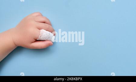 Main de bébé avec un doigt bandé sur un fond bleu de studio, espace de copie. Index blessé d'un enfant enveloppé dans un bandage blanc. Enfant garçon âgé o Banque D'Images