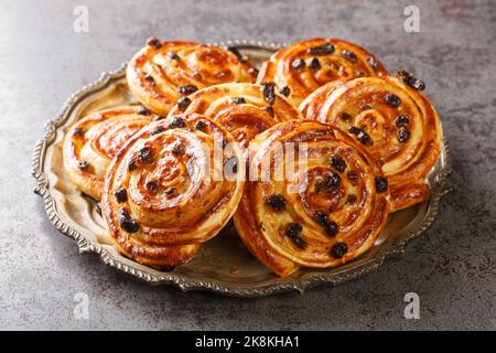 Petits pains à l'escargot faits maison avec raisins secs et crème anglaise dans une assiette. Horizontale Banque D'Images