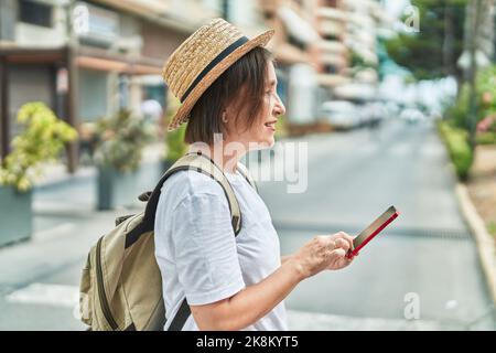 Femme d'âge moyen touriste souriant confiant en utilisant un smartphone dans la rue Banque D'Images