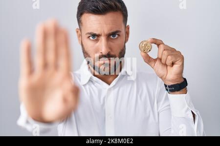 Beau hispanique homme tenant litecoin crypto-monnaie avec main ouverte faisant signe d'arrêt avec une expression sérieuse et confiante, geste de défense Banque D'Images