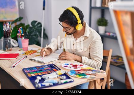 Jeune homme hispanique artiste à l'écoute de dessin de musique sur ordinateur portable dans un studio d'art Banque D'Images