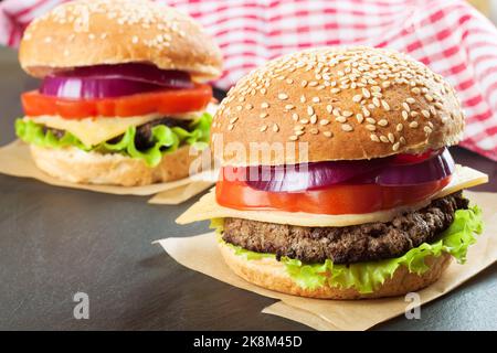 Deux cheeseburgers faits maison avec des viandes de bœuf et une salade fraîche sur des petits pains à l'assaisonnement, servis sur un tableau noir en ardoise. Banque D'Images