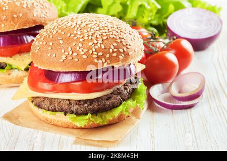 Cheeseburger maison avec viandes de bœuf, salade fraîche, tomates et oignons sur des petits pains à l'assaisonnement, servis sur une table en bois blanc. Banque D'Images