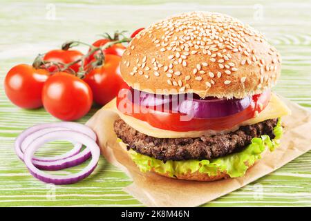 Cheeseburger maison avec viandes de bœuf, salade fraîche, tomates et oignons sur des petits pains à l'assaisonnement, servis sur une table en bois blanc. Banque D'Images