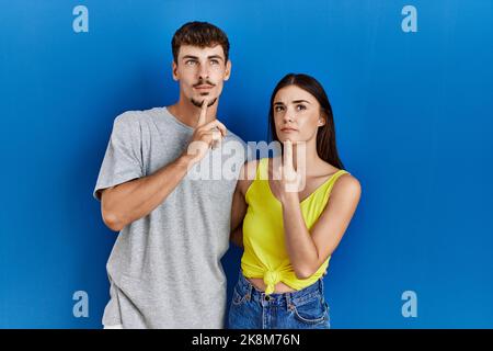 Jeune couple hispanique debout ensemble sur fond bleu pensant concentré sur le doute avec le doigt sur le menton et regardant vers le haut se demander Banque D'Images