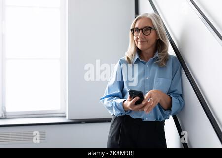 femme réussie de cinquante ans tête avec téléphone mobile dans le bureau Banque D'Images