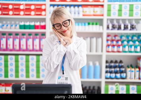 Jeune femme caucasienne travaillant à la pharmacie dort fatigué rêvant et posant avec les mains ensemble tout en souriant avec les yeux fermés. Banque D'Images