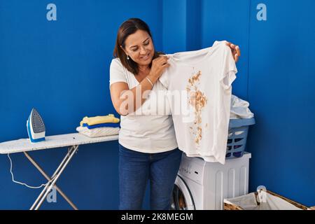 Femme hispanique d'âge moyen mettant la lessive sale dans la machine à laver expression sans indice et confuse. Doute concept. Banque D'Images