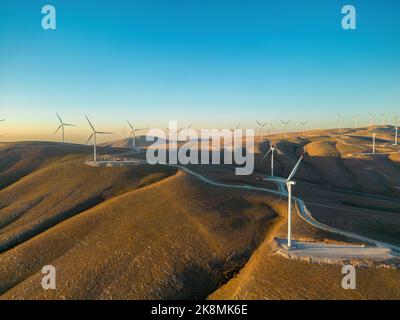 Vue aérienne de plusieurs éoliennes se tenant sur une colline et générant de l'électricité au lever du soleil Banque D'Images