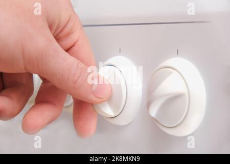 Un homme tourne la poignée d'un poêle à gaz blanc. Cuisinière à gaz blanc. Un homme allume un feu sur une cuisinière à gaz en tournant la poignée. Banque D'Images