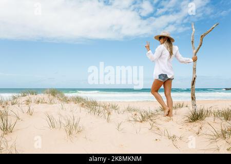 Femme portant une chemise blanche et impeccable sur une plage isolée avec du sable propre lors de belles vacances d'été. Bonne vibes et bois flotté Australie Banque D'Images