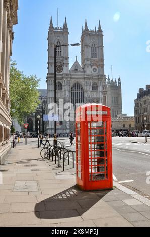 Un cliché vertical d'une cabine téléphonique rouge à Londres, au Royaume-Uni, avec des gens et le bâtiment de l'abbaye de Westminster en arrière-plan. Banque D'Images