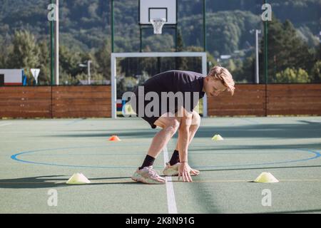 Un joueur de hockey actif se prépare pour la saison extérieure. Athlète blond sprint entre les cônes. Banque D'Images