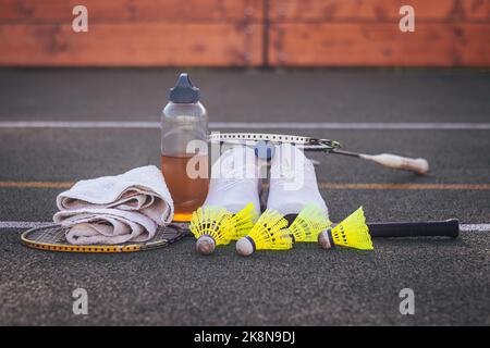 Équipement sportif pour une formation de qualité et un plaisir suffisants. Chauve-souris de badminton, serviette, boisson, baskets, balles de badminton. Terrain de sport en plein air. Banque D'Images