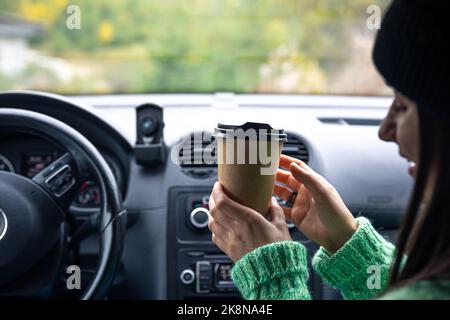 Une jeune femme avec une tasse de café s'assoit dans la voiture, concept de voyage. Banque D'Images