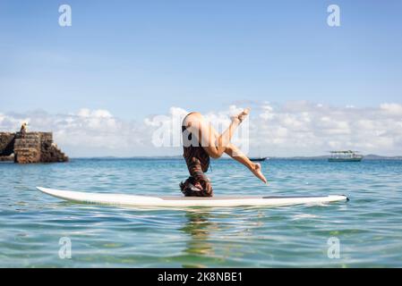 Salvador, Bahia, Brésil - 04 juin 2022: Une femme se dresse à l'envers sur une planche de surf à la plage de Porto da Barra à Salvador, Bahia. Banque D'Images