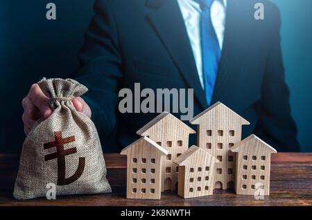 Un homme d'affaires met un sac d'argent en lire turque près des maisons. Industrie de la construction, entreprise de location et tourisme hôtelier. Investissements dans l'immobilier asse Banque D'Images