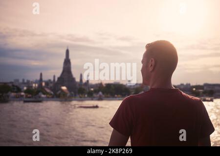 Vue arrière du touriste contre le paysage urbain avec la rivière Chao Phraya et Wat Arun au beau coucher du soleil. Bangkok, Thaïlande. Banque D'Images
