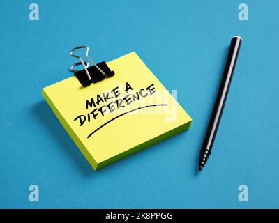 Le message fait une différence sur le papier autoadhésif jaune avec un stylo noir sur fond bleu. Banque D'Images