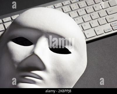 Masque facial blanc et clavier d'ordinateur sur fond noir. Pirate informatique, piratage informatique, cybercriminalité, escroquerie ou concept de sécurité en ligne. Banque D'Images