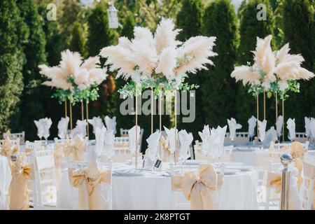 Le ruban s'encadre sur des chaises blanches autour de tables blanches à l'extérieur du lieu de réception de mariage Banque D'Images