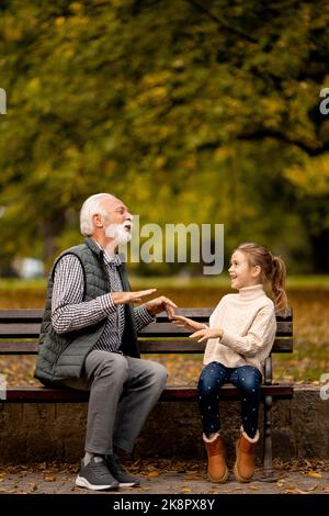 Beau grand-père jouant les mains rouges jeu de claquement avec sa petite-fille dans le parc le jour de l'automne Banque D'Images