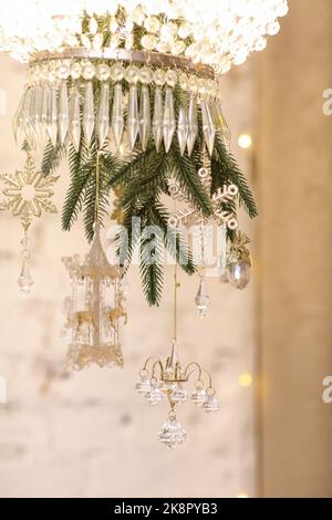 Gros plan sur un lustre en cristal de fête décoré de flocons de neige en verre, de boules dorées brillantes et de branches de sapin vert à l'intérieur du nouvel an. Chris Banque D'Images