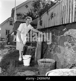 Kragerø 195406 - photos d'été de Kragerø. Une femme récupère de l'eau dans un poste d'eau à l'extérieur de sa maison. Godet. Baril. Eau potable. Photo: Actuel / NTB Banque D'Images