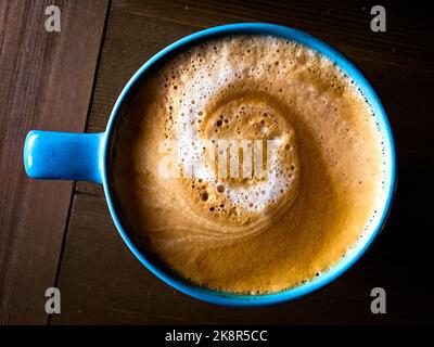 Vue de dessus d'un café cappuccino mousseux dans une tasse bleue sur une table en bois Banque D'Images