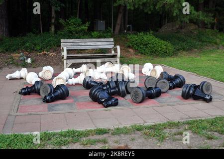 Pièces d'échecs qui ont été brocartées sur un plateau d'échecs extérieur Mega avec un banc en bois derrière. Banque D'Images