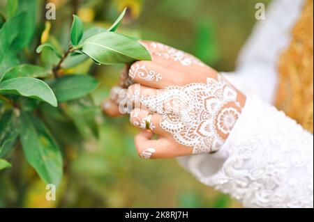 Un gros plan des mains de mariée avec de beaux mehendi de mariage touchant les feuilles vertes Banque D'Images