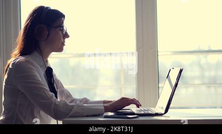 Vue latérale de la femme attentionnée ciblée avec succès répartiteur, port de casque , regarde l'écran, travail sur un ordinateur, ordinateur portable dans le bureau. L'opérateur du centre d'appels, ou l'éducation sur le Web, consulte le client par vidéo. Photo de haute qualité Banque D'Images