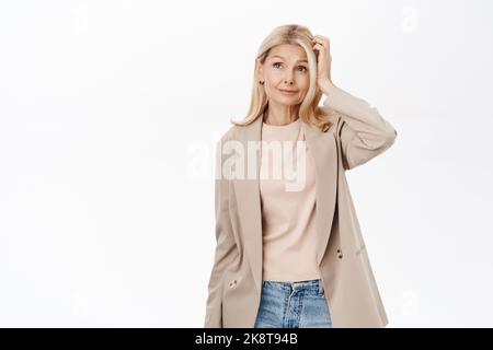 Portrait d'une femme blonde d'âge moyen, la femme mûre semble confuse, perplexe par la gite, la pensée, debout sur fond blanc Banque D'Images