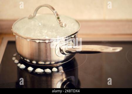 Porridge de lait versé pendant l'ébullition de sous le couvercle de la casserole sur un poêle à induction électrique Banque D'Images