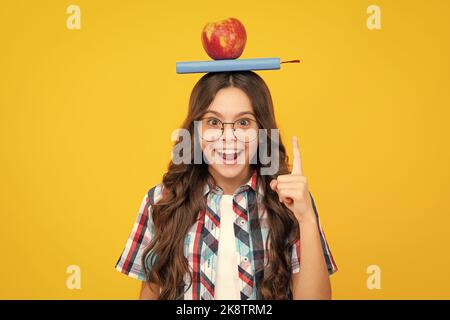 Retour à l'école. Adolescente avec pomme sur la tête, prête à apprendre. Les écoliers sur fond jaune isolé. Banque D'Images